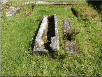 Stone coffin with its lin in the grass next to it