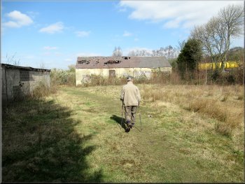 Path across a rough field with two derelict buildings