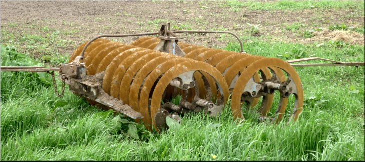 A type of disc harrow in a field by the lane